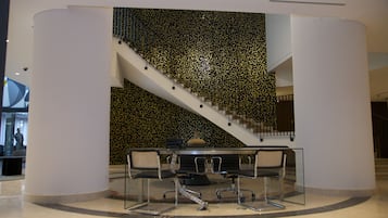 Un interior moderno con una escalera, una mesa de vidrio y sillas, y una pared decorativa.