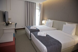 Habitación de hotel con dos camas, un escritorio, un televisor y una ventana con cortinas.