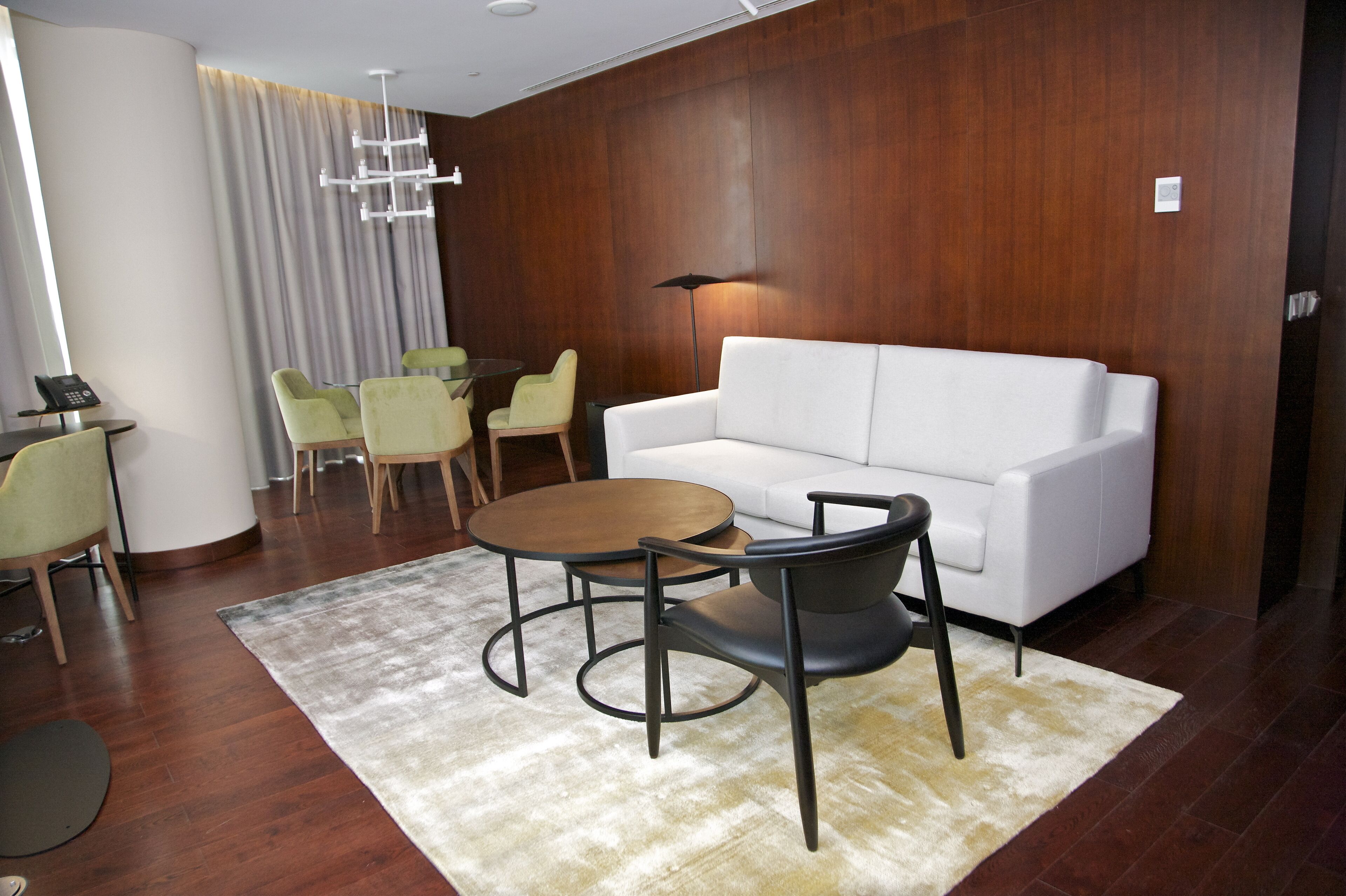 A modern hotel room with a white sofa, a round wooden table, and four chairs.