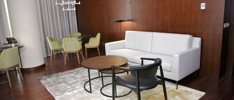 A modern hotel room with a white sofa, a round wooden table, and four chairs.