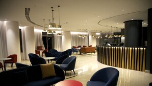 A modern hotel lobby with blue armchairs, a red table, and a reception desk. - Hotel Continental Horizonte (Luanda)