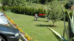 A garden with a cart, a car, and a person holding a plant. - Pension Wirt am Bach (Terento)