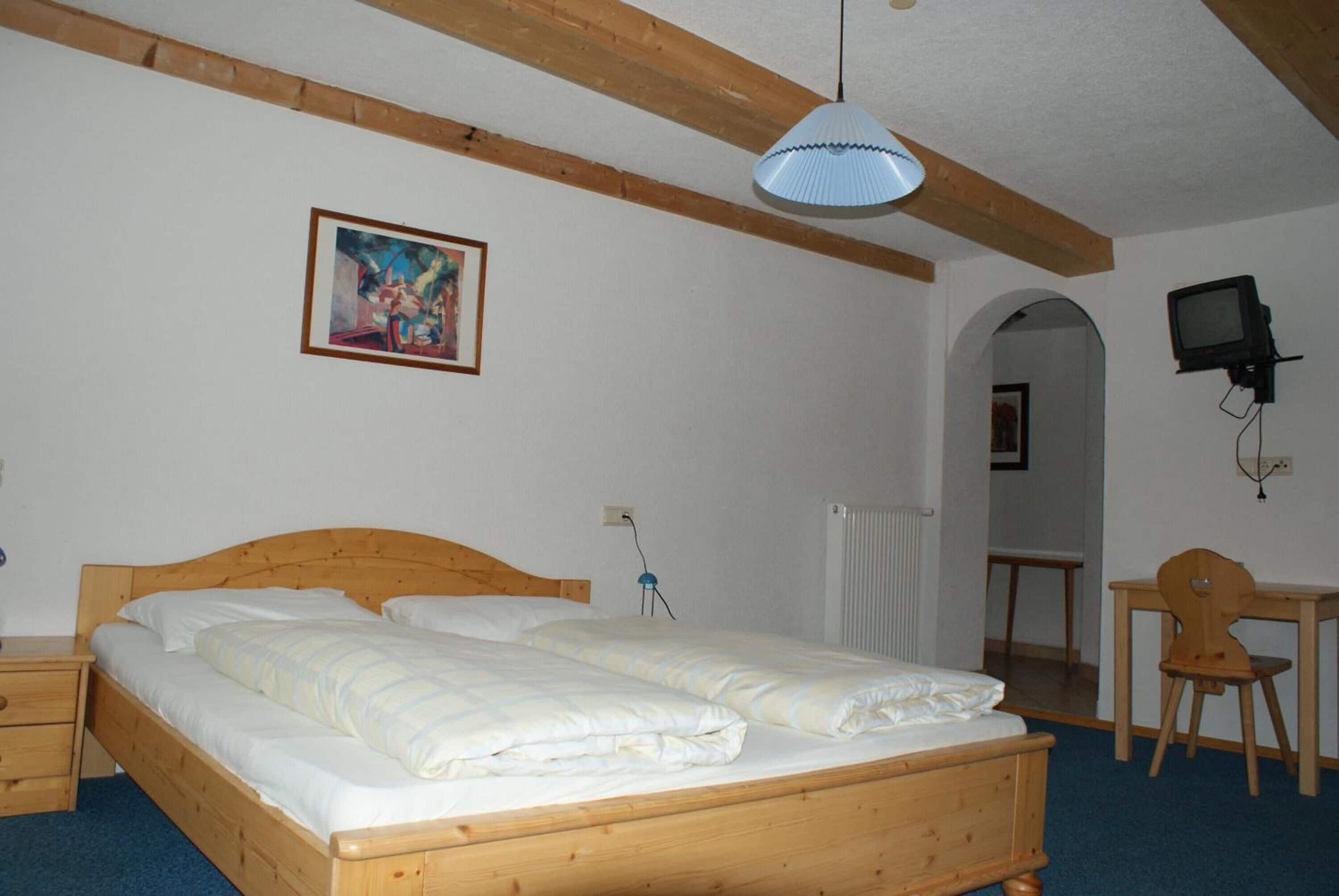 Un dormitorio con una cama de madera, un escritorio, una silla, un televisor y un cuadro en la pared.