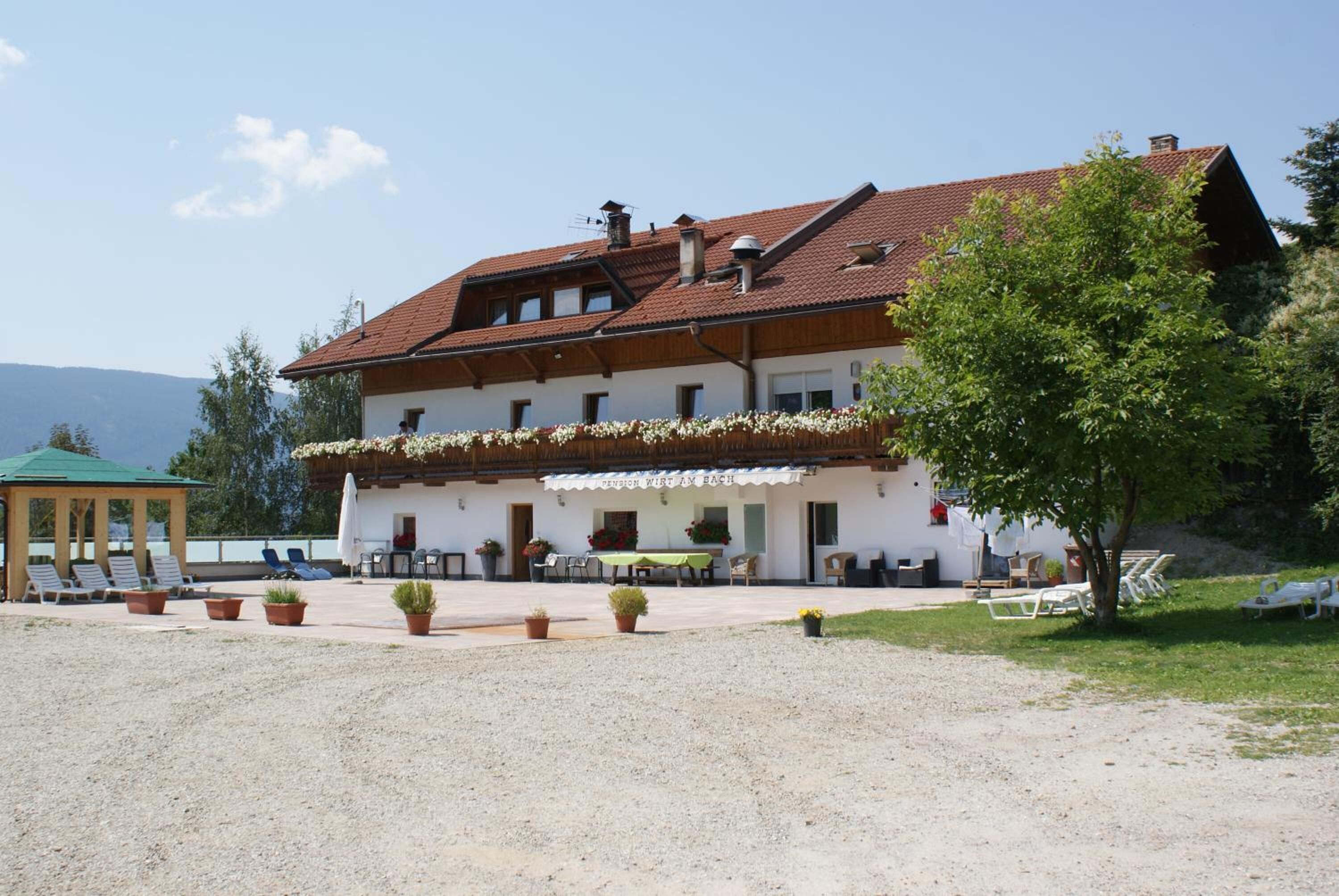 A two-story building with a red-tiled roof, outdoor seating area, and a covered gazebo.