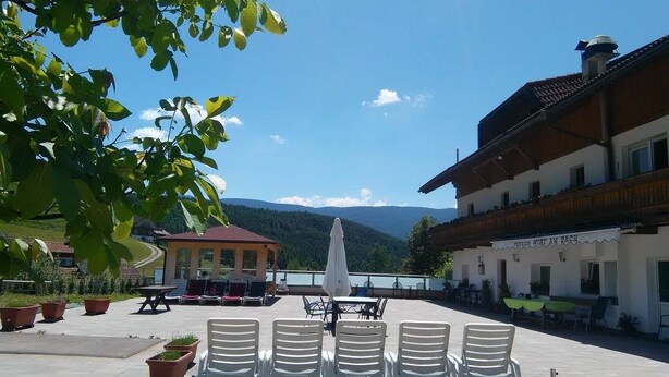 An outdoor seating area with tables and chairs, a gazebo, and a building with a sign that reads "Pension Wirt am Bach". - Pension Wirt am Bach (Terento)