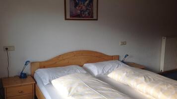 Une chambre avec une tête de lit en bois, deux lits simples avec du linge de lit blanc, une table de chevet avec une lampe et un tableau au mur.