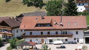 A multi-story building with a red-tiled roof, balconies, and outdoor seating areas. - Pension Wirt am Bach (Terento)