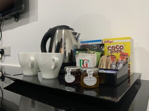 Eine Küchenarbeitsfläche mit einer Kaffeemaschine, zwei weißen Tassen, Honiggläsern, einer Packung Kellogg's Coco Pops, einer Packung PG Tips Tee und einer Zuckerdose.