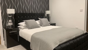 A modern bedroom with a black upholstered bed, two bedside tables with lamps, a patterned wall, and a neutral color scheme. - Your Oxford Stay (Oxford)