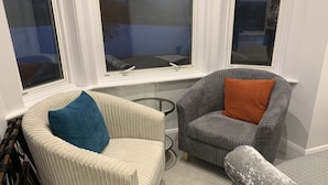 A room with two armchairs, one with a blue pillow and the other with an orange pillow, positioned near a window with a view of trees. - Your Oxford Stay (Oxford)
