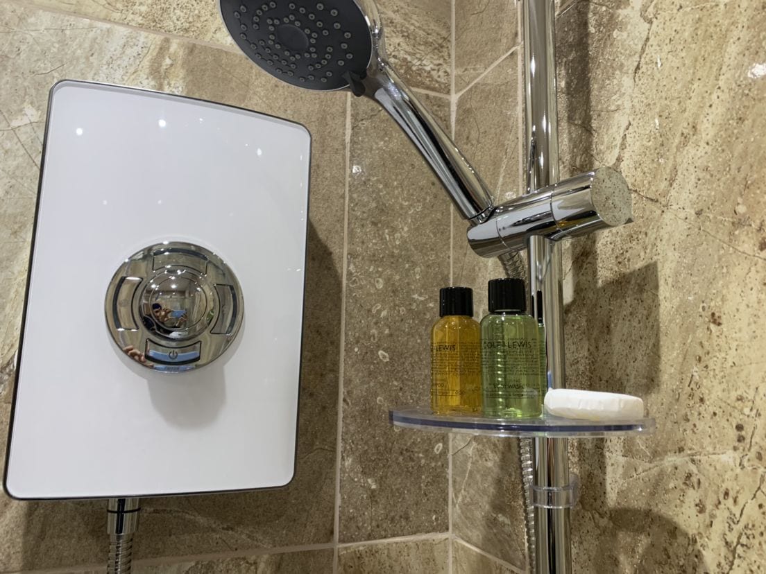 A shower with a chrome faucet, a handheld showerhead, and two bottles of liquid soap on a clear shelf.