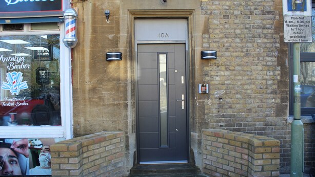A traditional barber shop with a dark-colored door marked "10A" and a sign indicating a waiting limit of 1 hour. - Your Oxford Stay (Oxford)