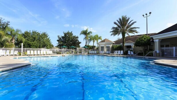 A clear blue swimming pool with lounge chairs and umbrellas, surrounded by palm trees and a building with a covered patio. - Ov2571 - Windsor Palms Resort - 4 Bed 3 Baths Townhome (Kissimmee)