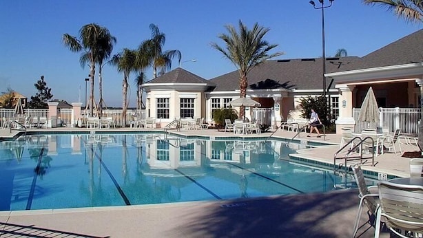 A swimming pool with lounge chairs and palm trees, surrounded by buildings with a classic architectural style.