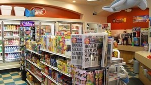 A grocery store interior with shelves stocked with various products, a refrigerated section, and a checkout area.