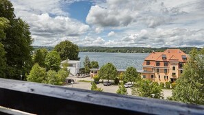 A lakeside view with a hotel featuring a red roof, a parking area, and lush greenery. - Hotel Schloss Berg (Berg)