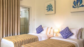Une chambre d’hôtel avec deux lits, une porte vitrée donnant sur une salle de bain et des œuvres d’art accrochées aux murs.