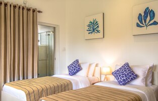 A hotel room with two beds, a glass door leading to a bathroom, and artwork on the walls.