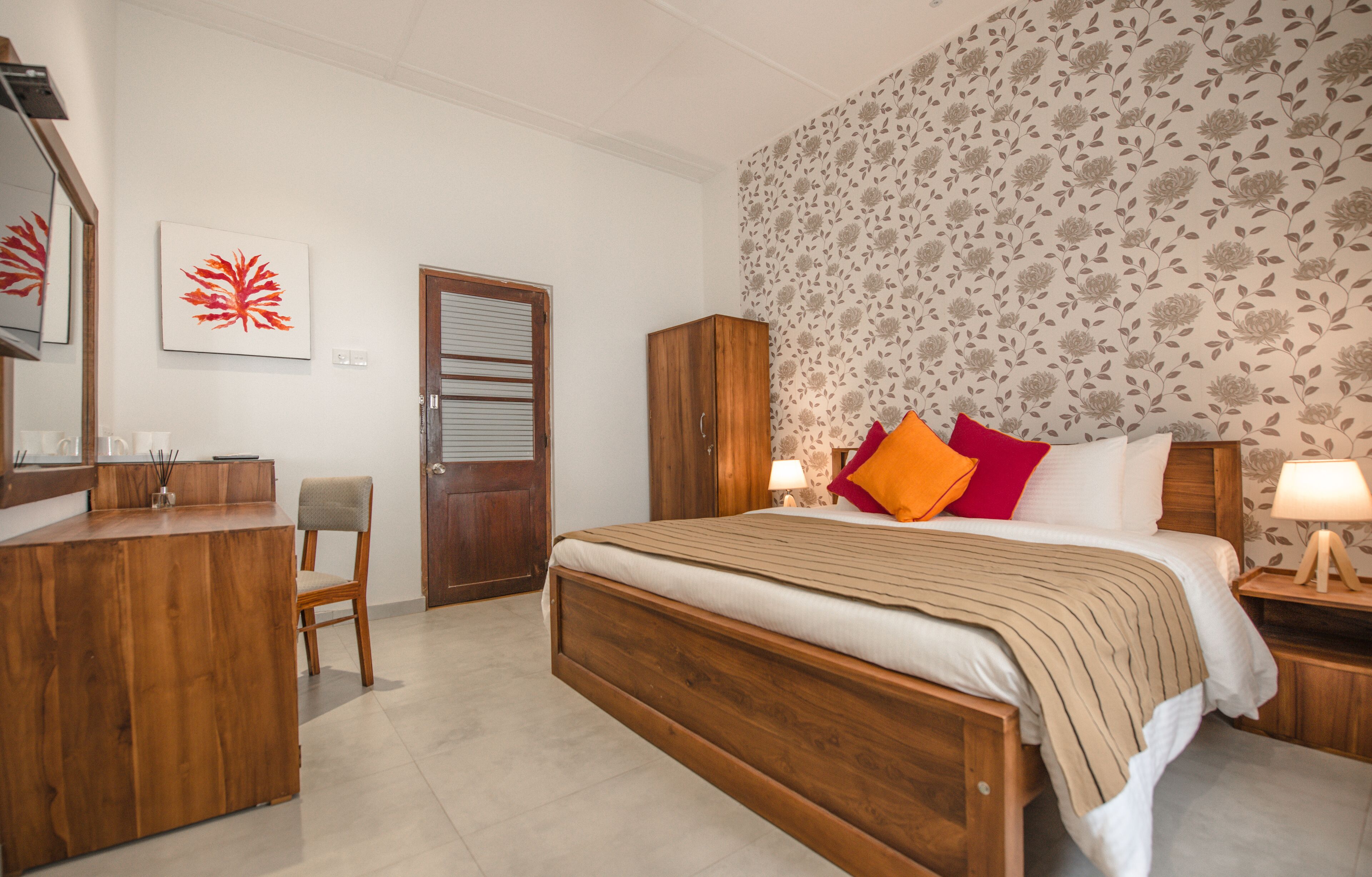Ein Schlafzimmer mit einem hölzernen Bett, einem Schreibtisch, einem Stuhl, einem Kleiderschrank und blumigem Tapetenmuster.