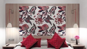 A hotel room with a bed, two red pillows, a nightstand, a lamp, and a wall with a floral pattern. - Hotel Ginebra (Barcelona)
