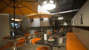 A restaurant with orange chairs, black tables, and yellow umbrellas. - Hotel Ginebra (Barcelona)