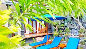 A patio area with wooden lounge chairs and a table, surrounded by greenery and a decorative rock wall. - Toro Cottage (Penida Island)
