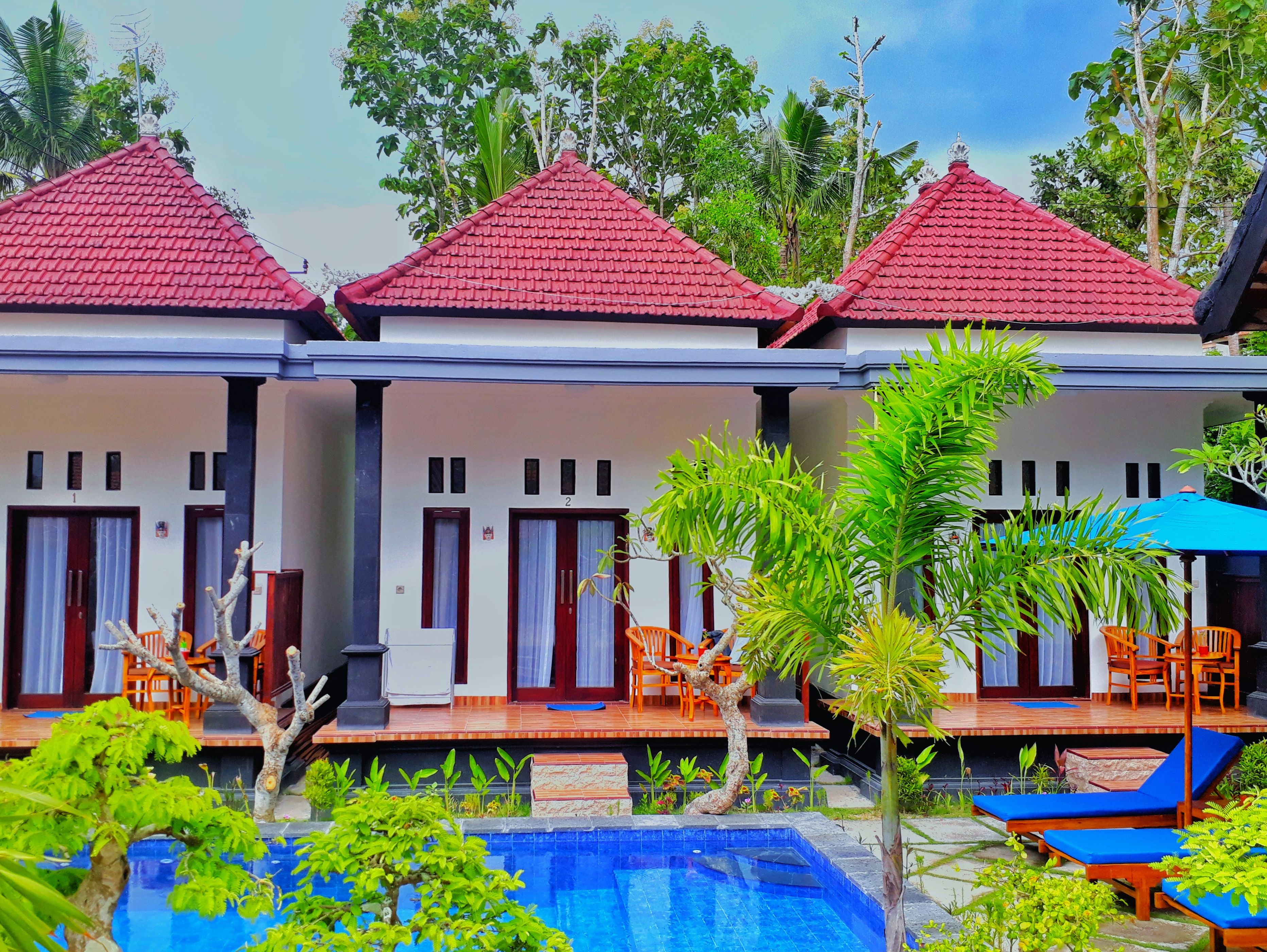 A hotel with three red-roofed buildings, each with a balcony and a pool area.