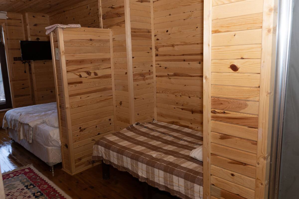 A wooden cabin room with a bed, a bench, and a television.