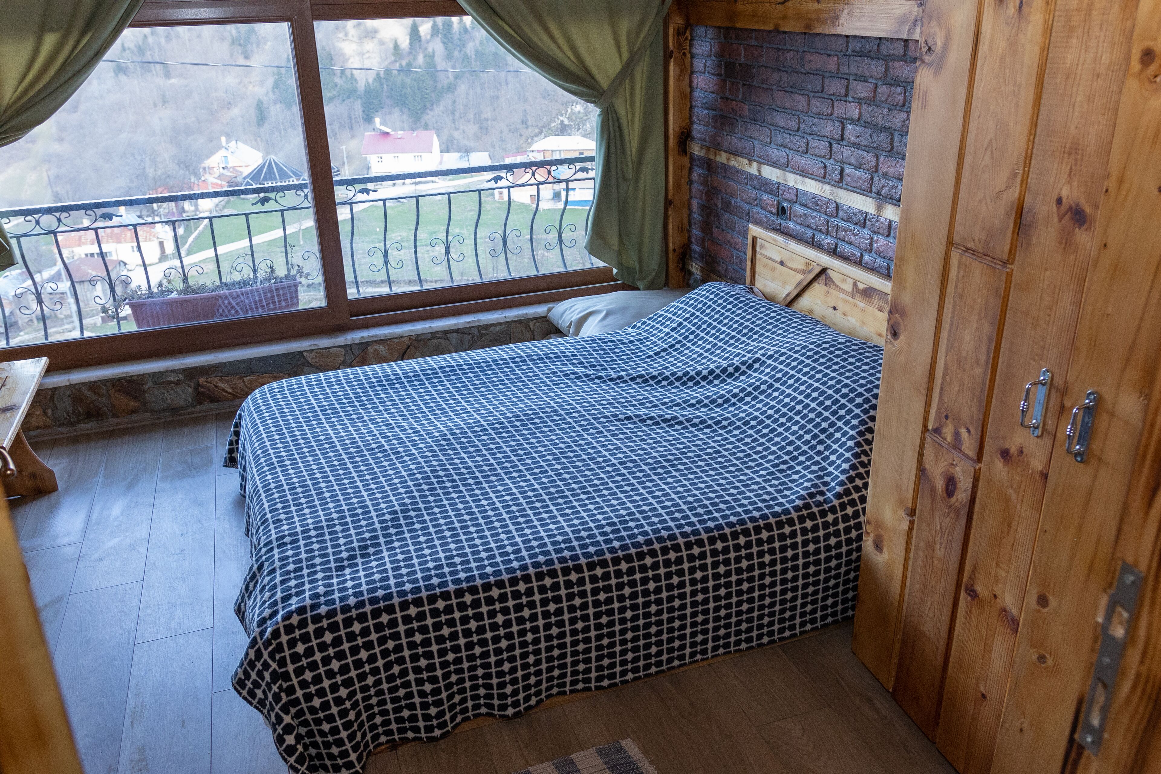 A bedroom with a bed, a window with curtains, a brick fireplace, and a balcony with a railing.