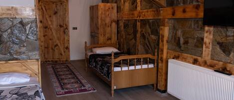 Une chambre à coucher en bois avec un mur en pierre, un lit, une table de chevet, une commode et un téléviseur fixé au mur.