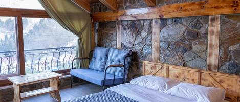 Una habitación acogedora con una cama, un banco de madera y una silla. Las paredes son de piedra y el techo de madera.