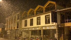 Un edificio de dos pisos con el suelo cubierto de nieve, amplias ventanas y un escaparate visible con mesas al aire libre.