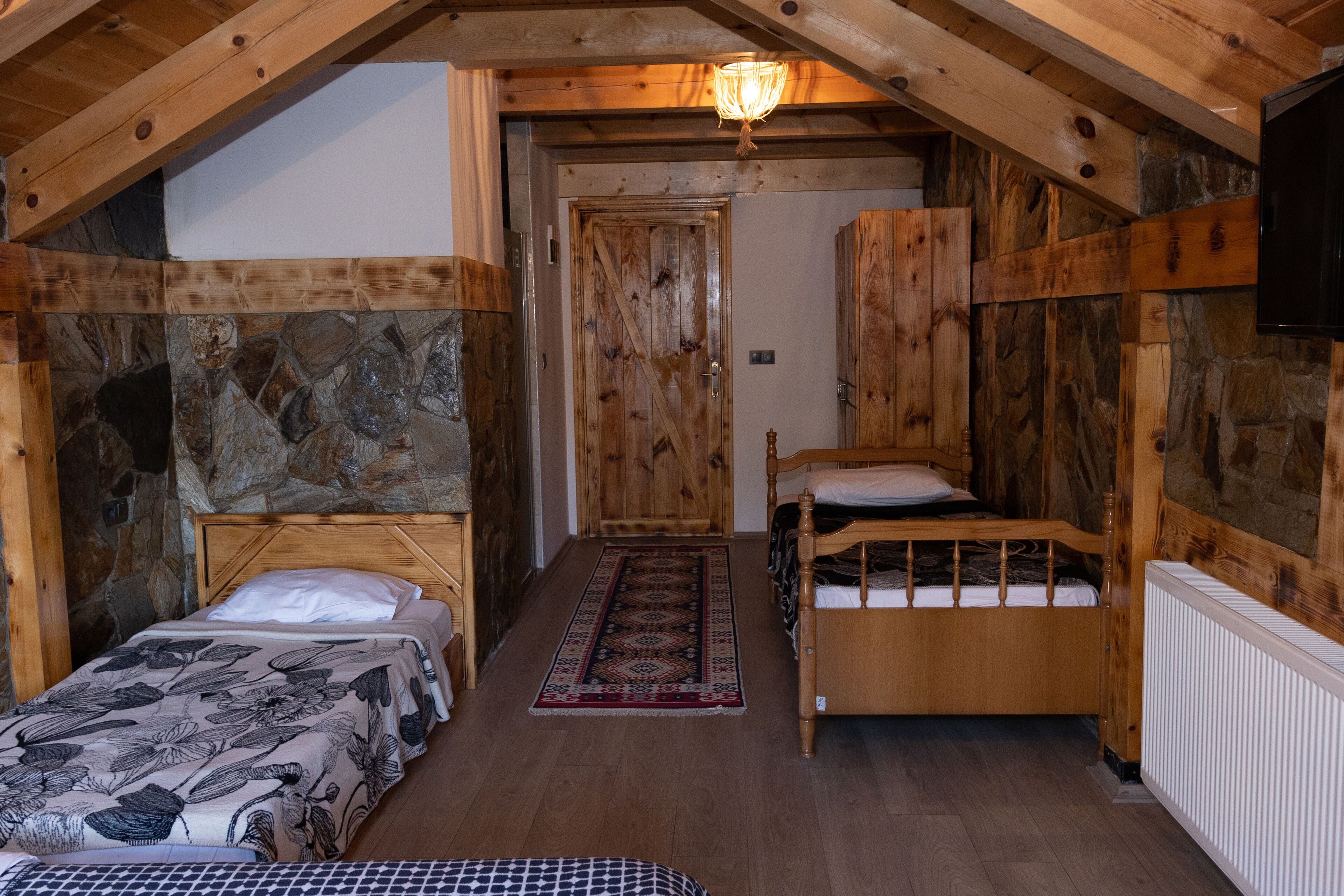 Una habitación rústica de madera con dos camas, un muro de piedra y techo de madera.