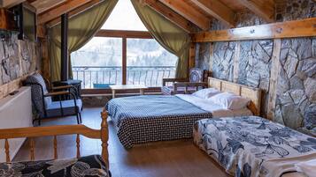 Una cabaña acogedora con interior de madera, una pared de piedra, una cama con ropa de cama floral, un escritorio y vistas a las montañas.
