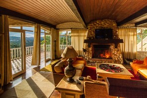 Un salón acogedor con chimenea de piedra, asientos cómodos y un amplio ventanal con vistas a un paisaje pintoresco.
