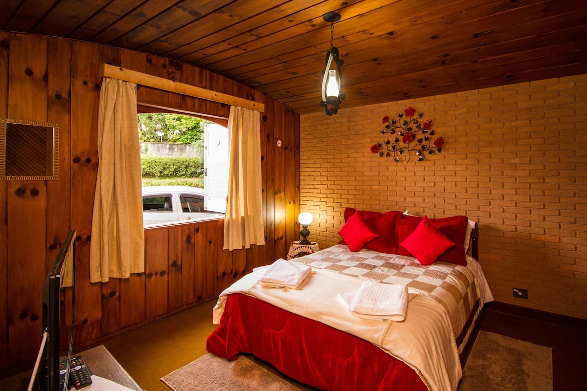 Quarto de cabana de madeira com cama, mesa de cabeceira, abajur e janela com cortinas.
