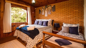 A wooden cabin bedroom with two beds, a large window, and a brick wall. - Pousada Déjà Vu (Campos do Jordão)
