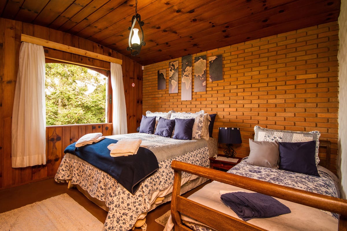 Quarto de cabana de madeira com duas camas, uma janela grande e uma parede de tijolos.
