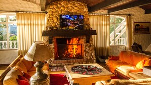 A cozy living room with a stone fireplace, a television, and comfortable seating. - Pousada Déjà Vu (Campos do Jordão)