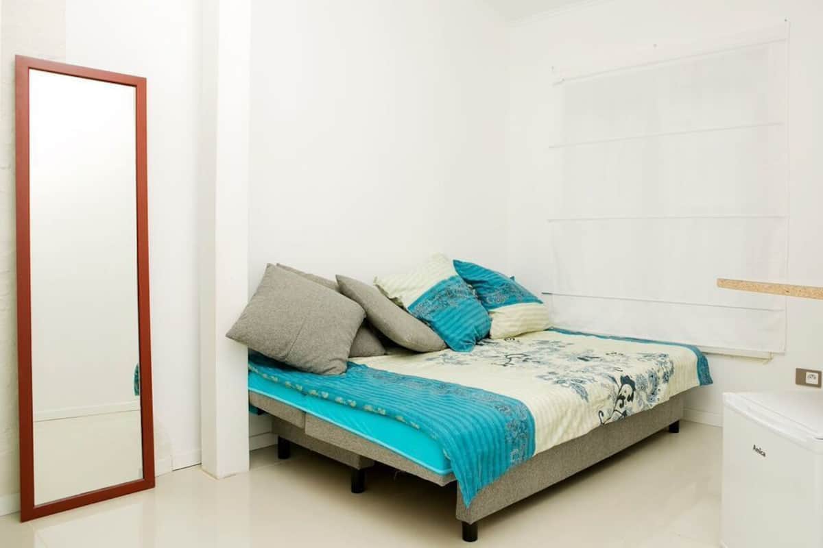 A bedroom with a bed, pillows, a blanket, a wardrobe, and a small white appliance.