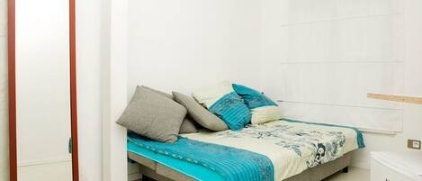 A bedroom with a bed, pillows, a blanket, a wardrobe, and a small white appliance.