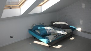A bedroom with a skylight, a bed with blue bedding, and a white brick wall. - Studio Rental Central Warsaw (Warsaw)