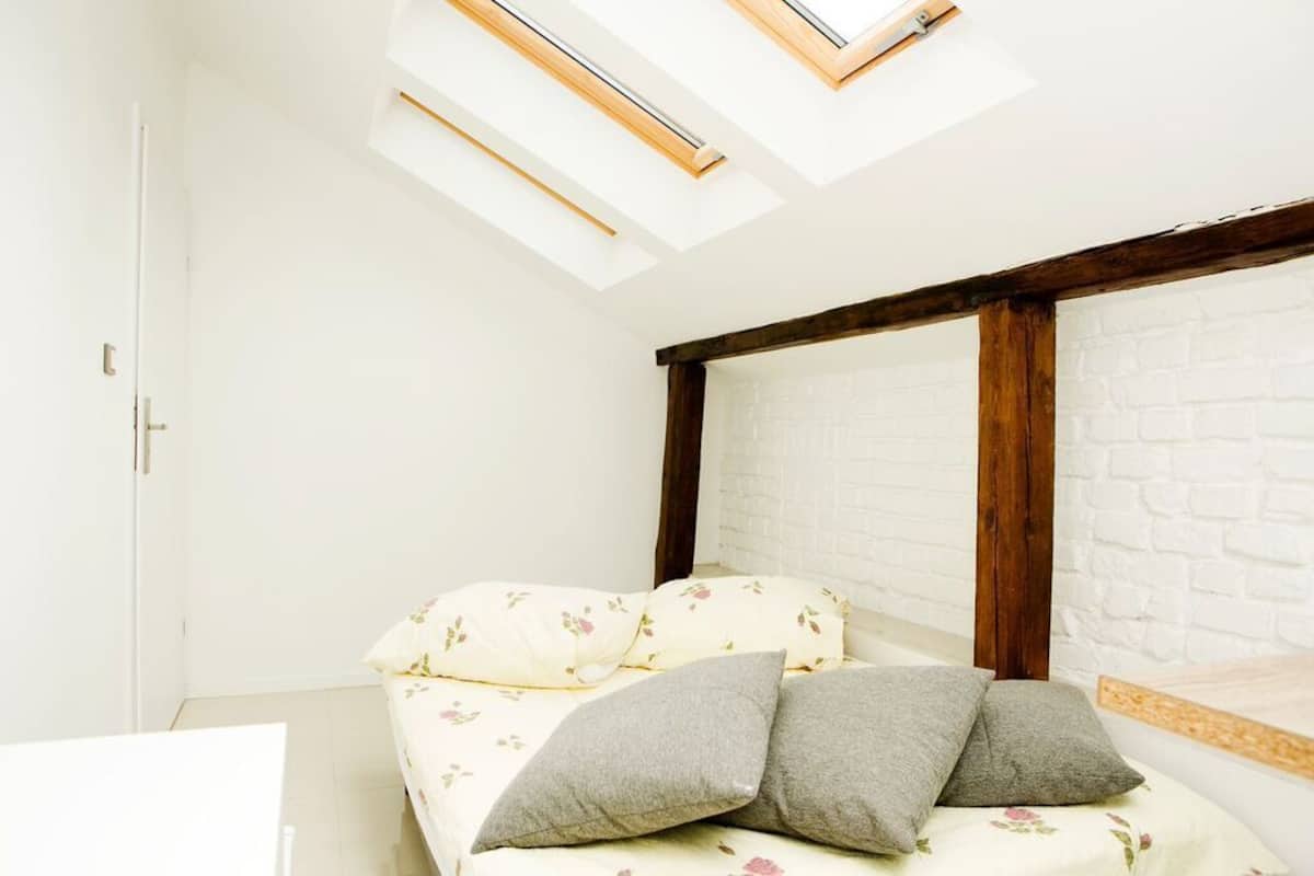 A room with a bed, skylights, a white brick wall, and a wooden beam structure.