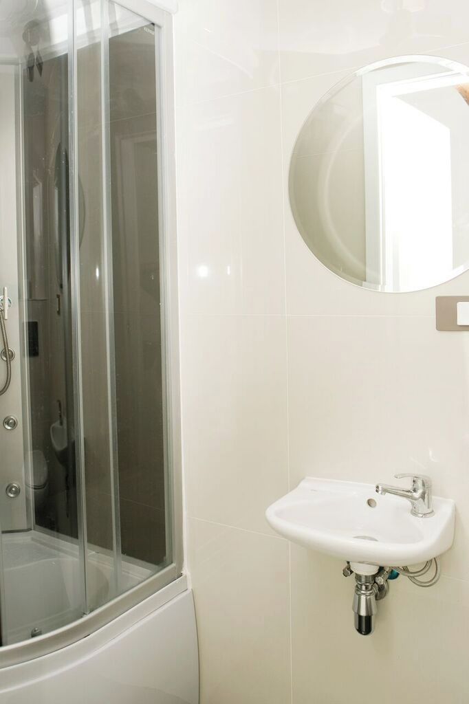 Un baño con ducha de vidrio, un lavamanos blanco y un espejo redondo.