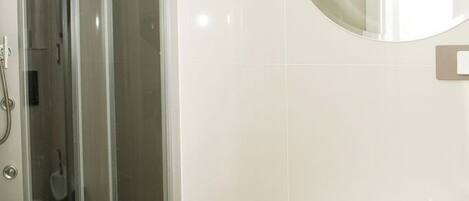 Un baño con ducha de vidrio, un lavamanos blanco y un espejo redondo.