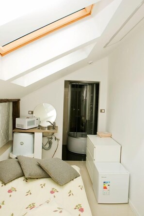 A compact bedroom with a skylight, a bed with floral bedding, a white refrigerator, a microwave, and a small sink. - Studio Rental Central Warsaw (Warsaw)