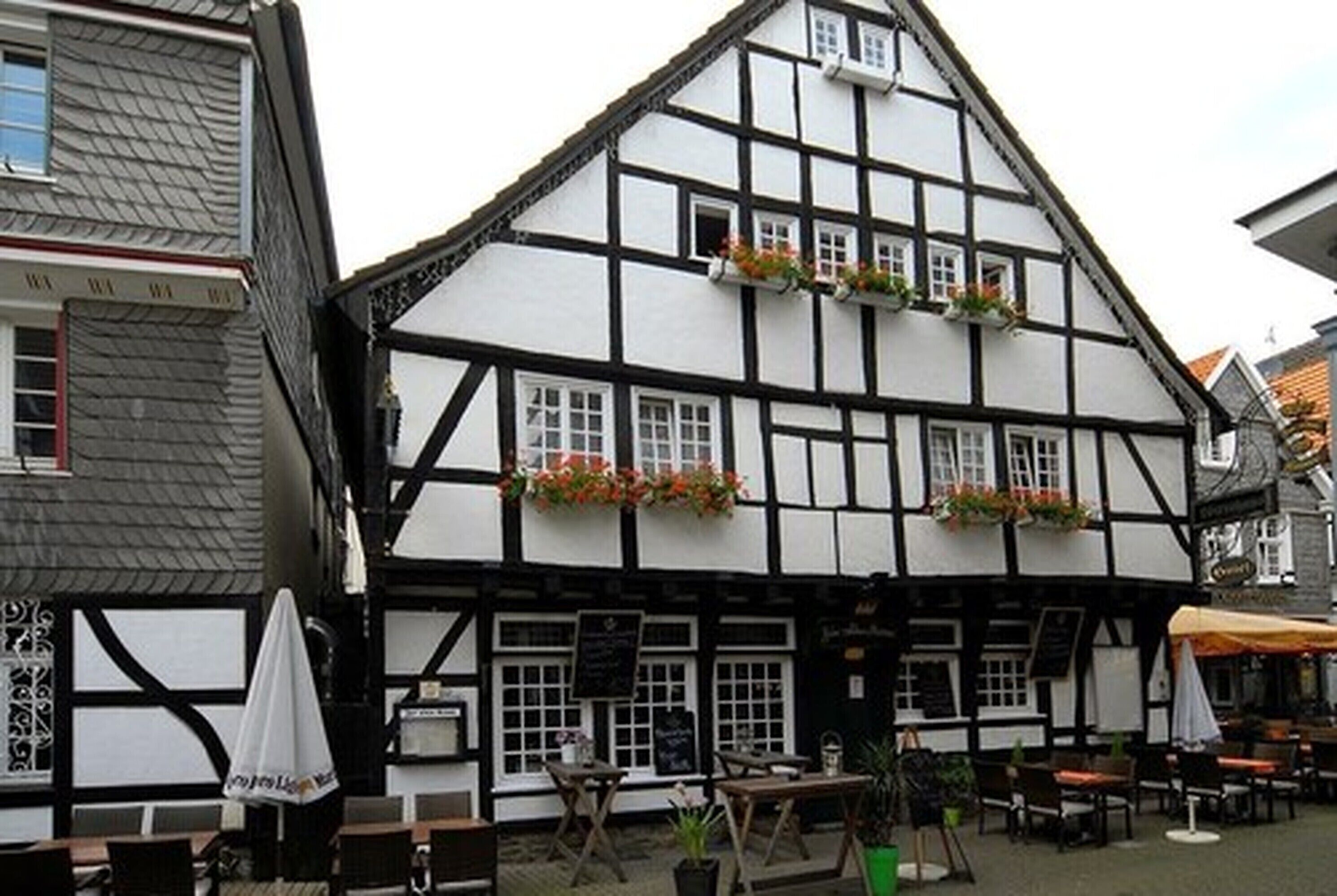 Un edificio tradicional de entramado de madera con múltiples ventanas, mesas al aire libre y macetas con flores.
