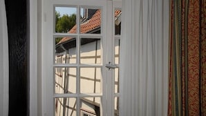 A room with a white door with glass panels, a view of neighboring buildings, and a patterned curtain. - Zur alten Krone (Hattingen)