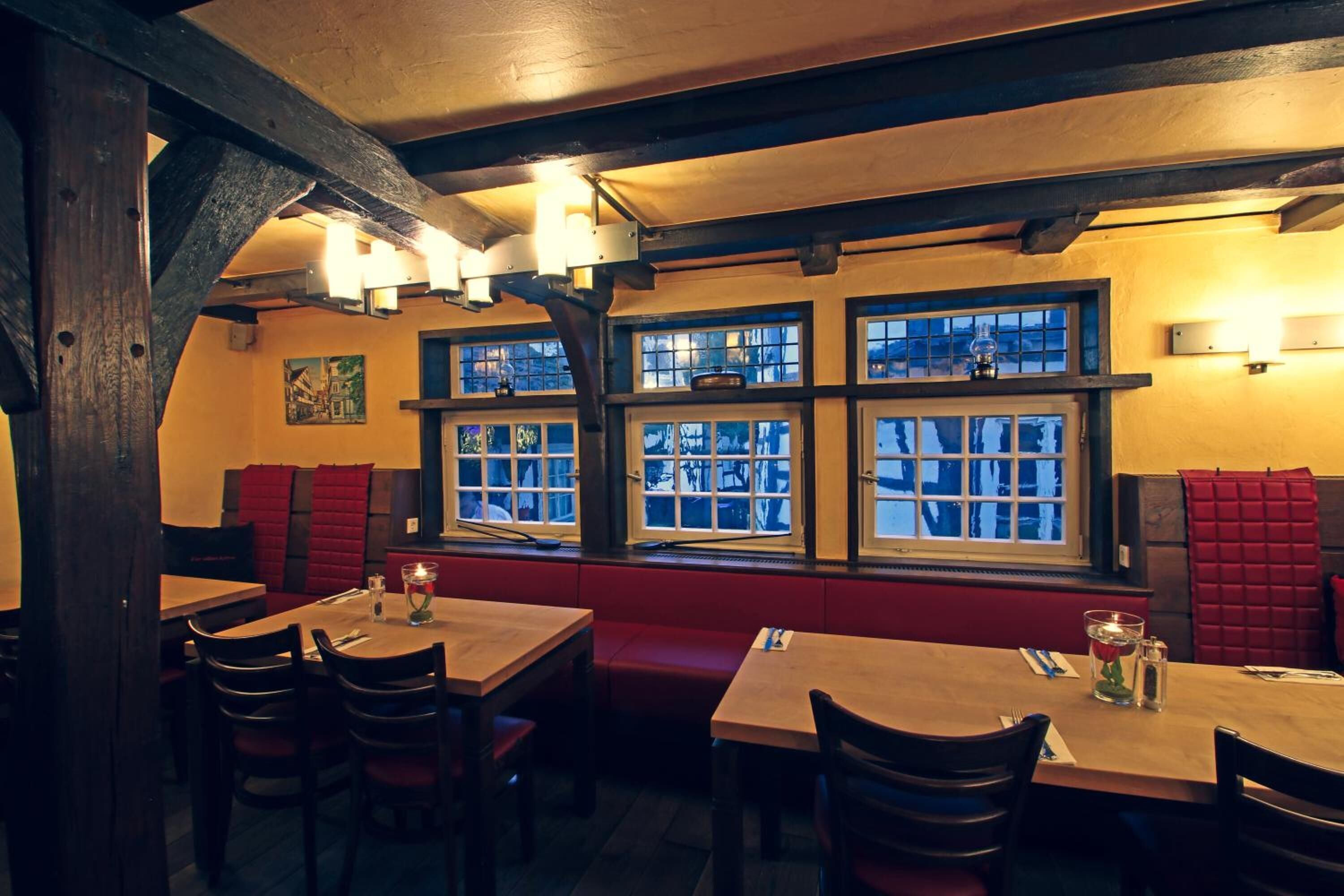 A cozy restaurant with wooden tables and benches, large windows with views, and warm lighting.