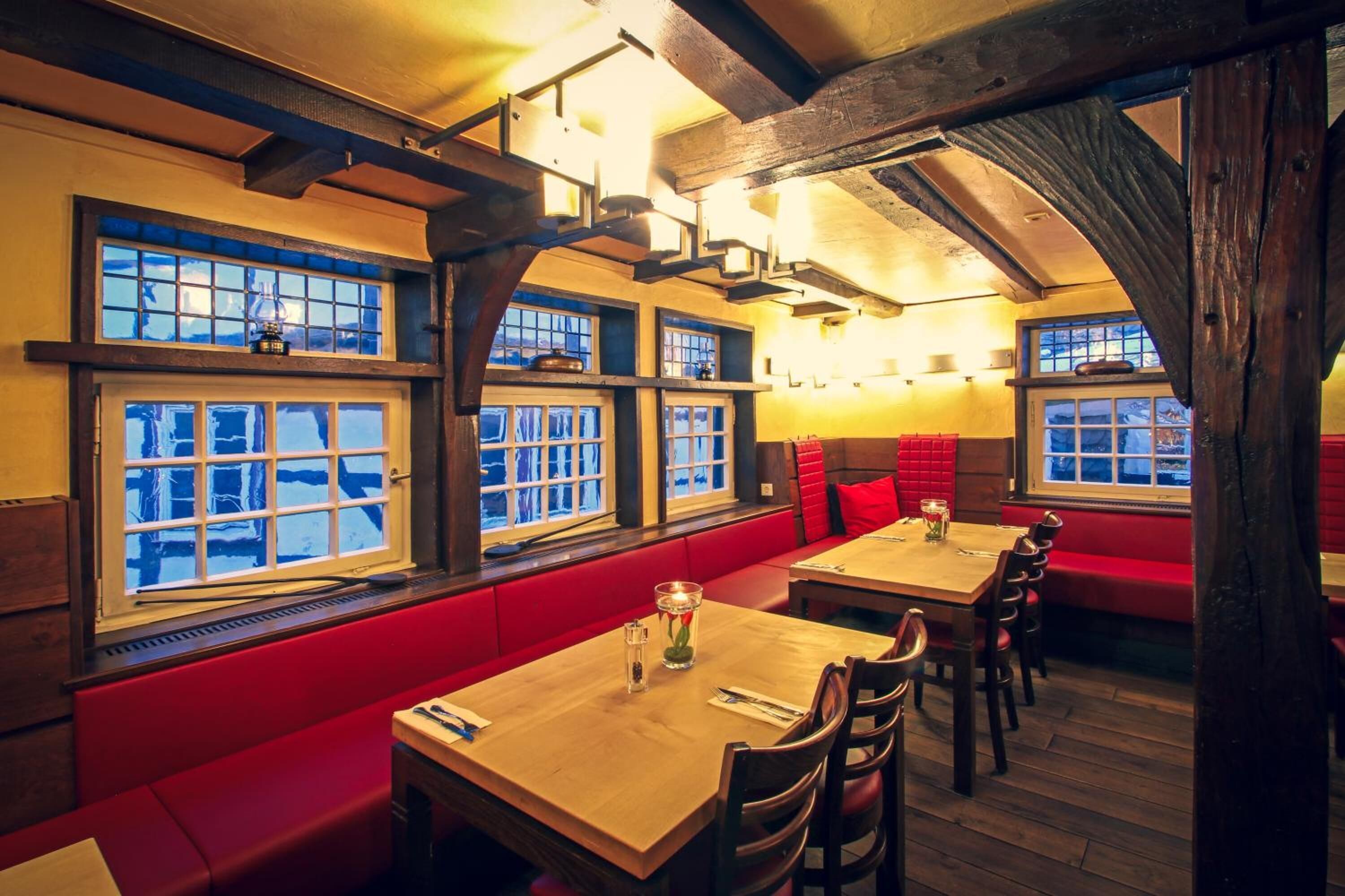 Un restaurante con mesas de madera y bancos acolchados rojos.